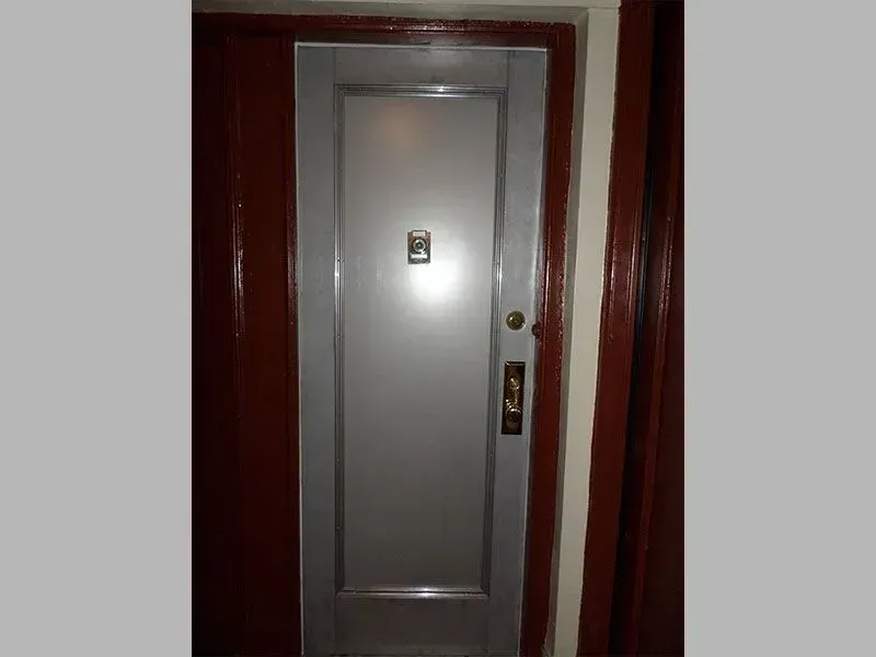 Silver door with a doorbell, handle, and a single pane. Brown door frame.