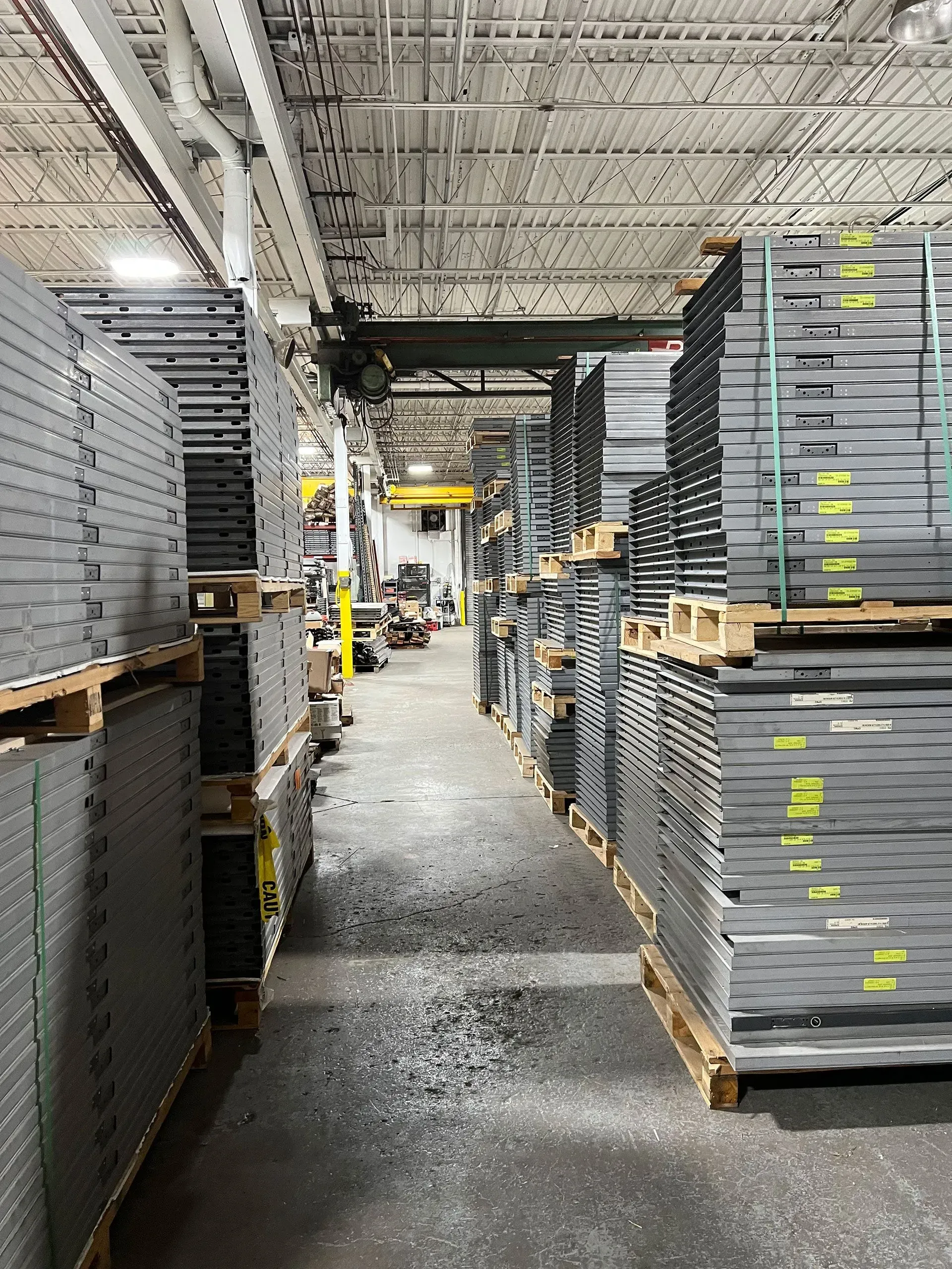 Warehouse aisle with stacked pallets of gray and black material, overhead crane.