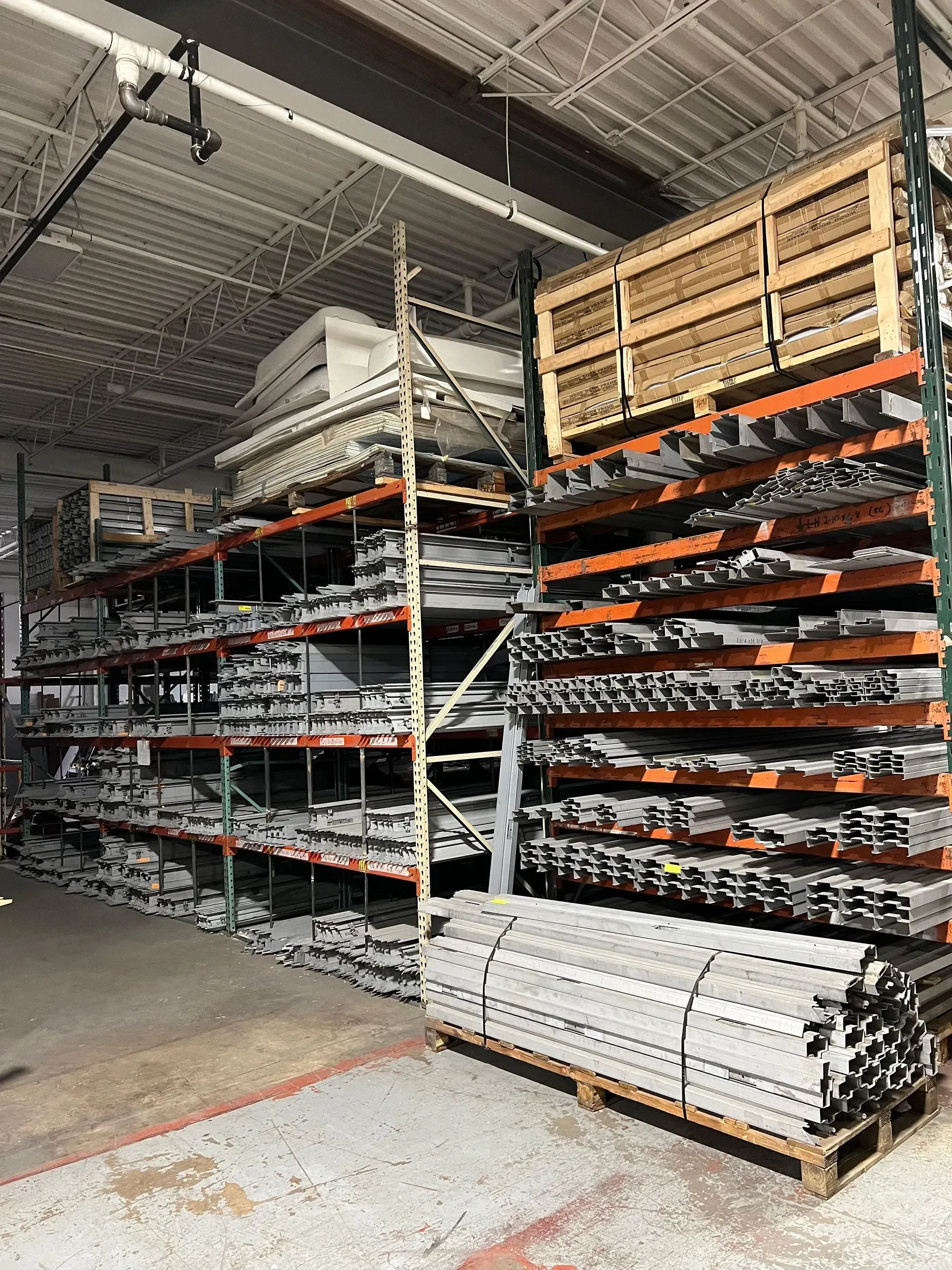 Shelves stacked with metal materials in a warehouse setting. Pallet of pipes at the front.