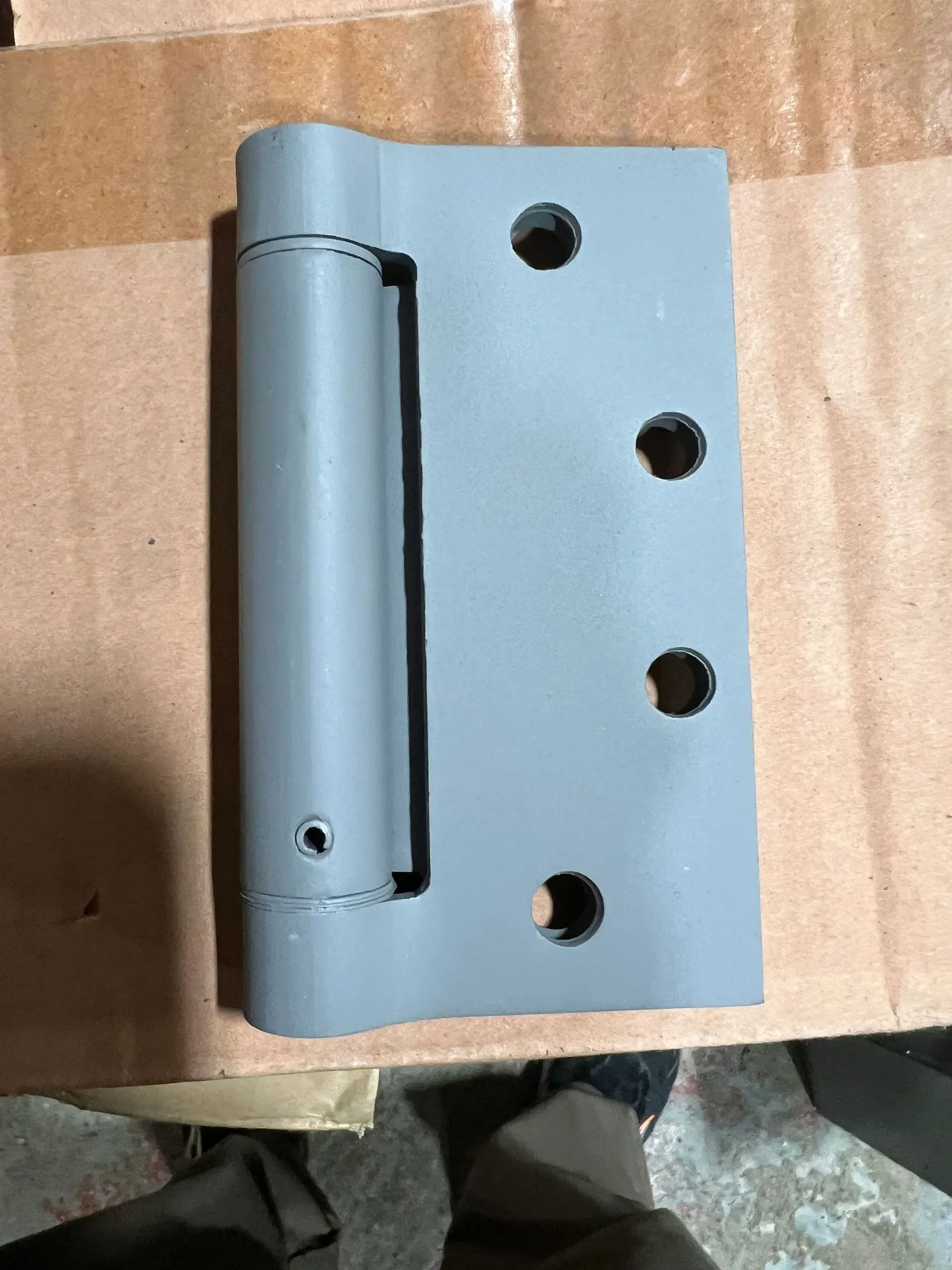 Gray spring hinge with screw holes.