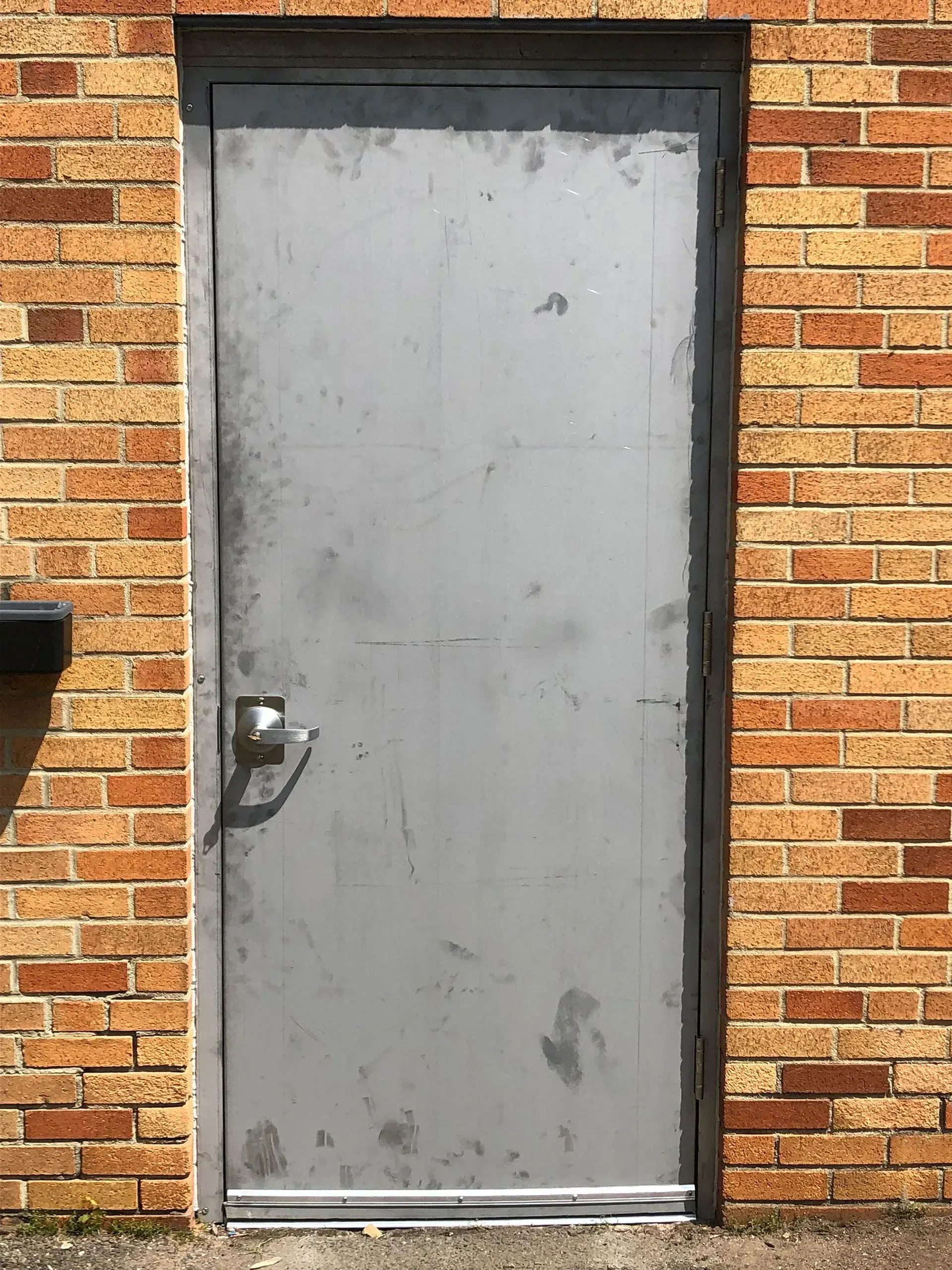 Gray metal door in brick wall with handle.