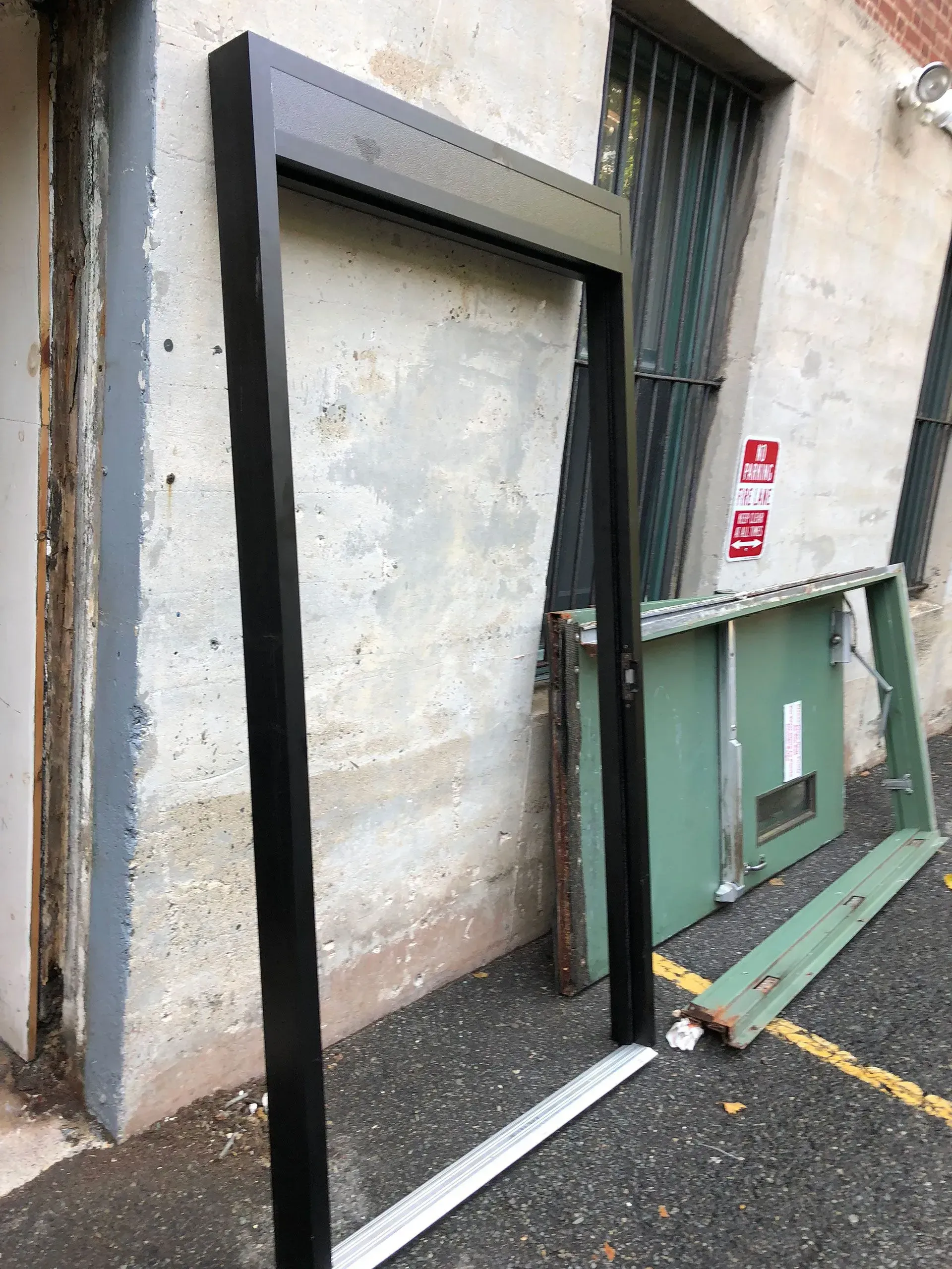 Black door frame leaning against a weathered concrete wall near a green door and debris.