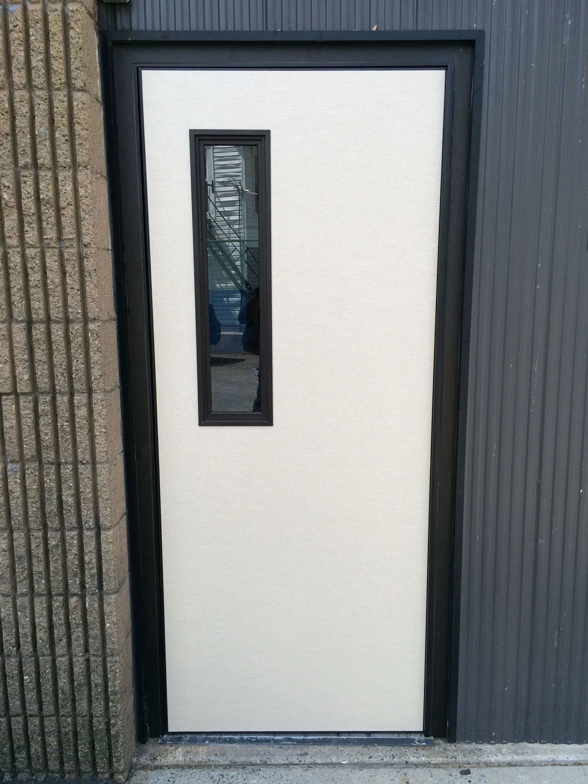 White textured door with a black frame and narrow rectangular window.