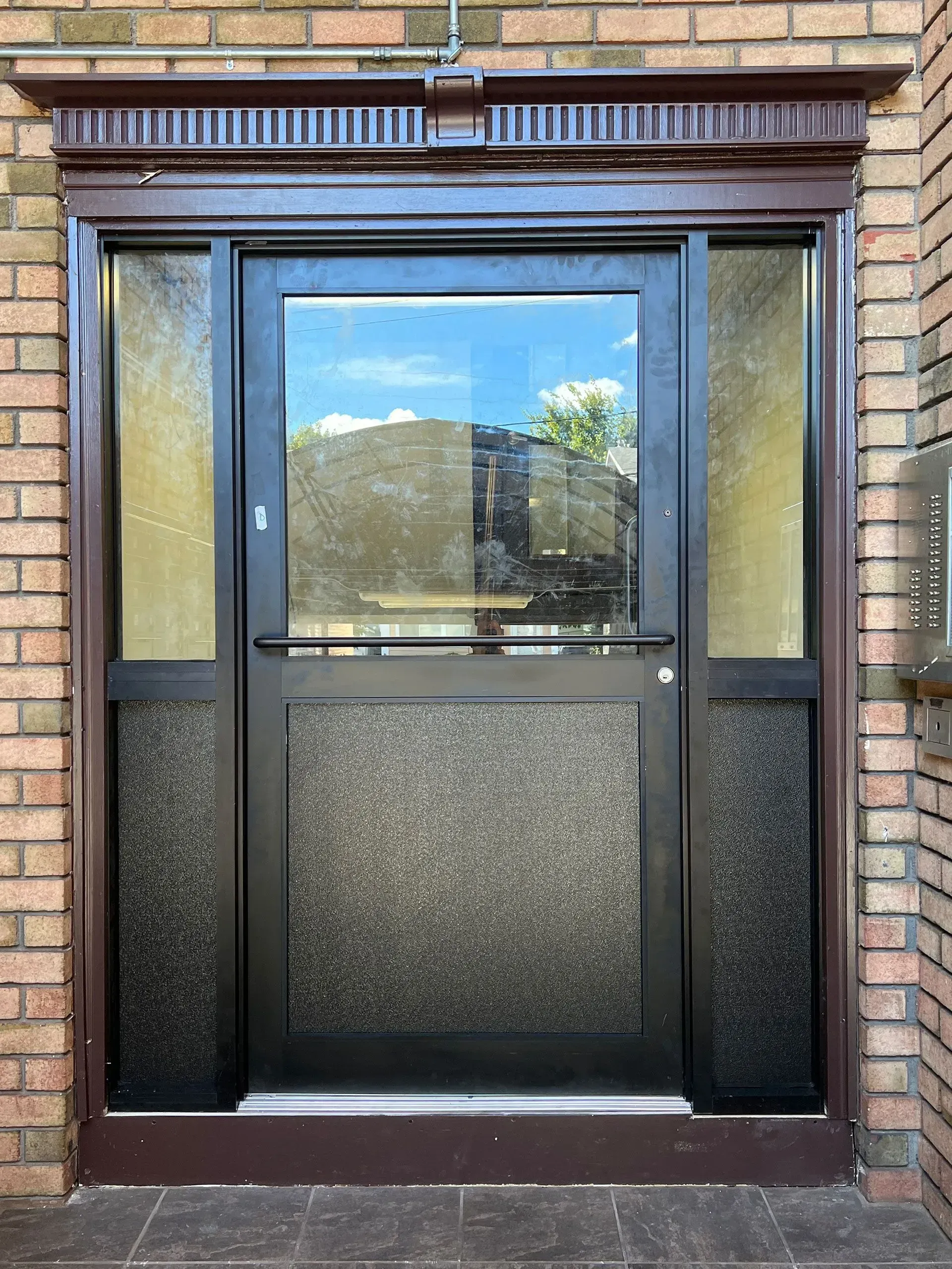 Brown-framed entrance door with clear and textured glass panels, set in brick.