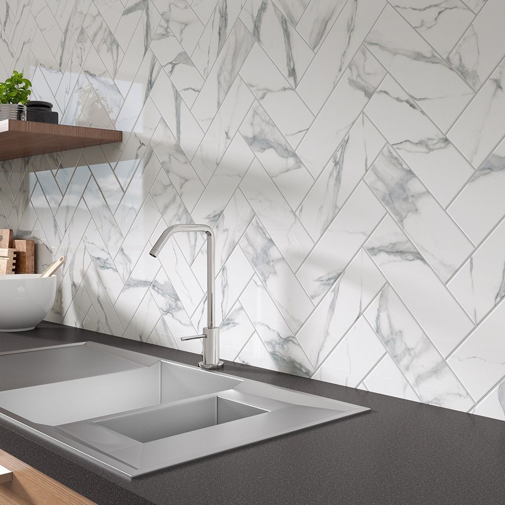 A kitchen with a sink , faucet , and marble tiles on the wall.
