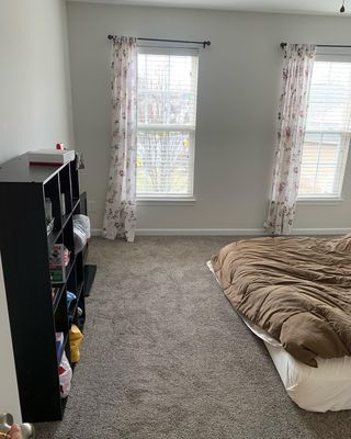 A bedroom with a bed , bookshelf , and two windows.