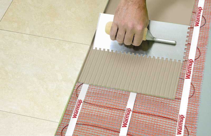 A person is laying tiles on a floor with a trowel.