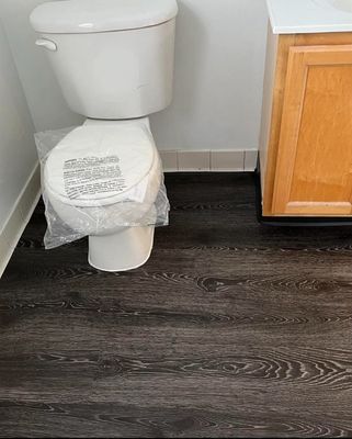 A toilet is sitting on a wooden floor in a bathroom next to a sink.