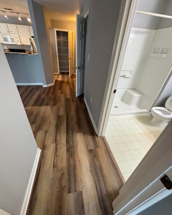 A hallway with hardwood floors leading to a bathroom and kitchen.