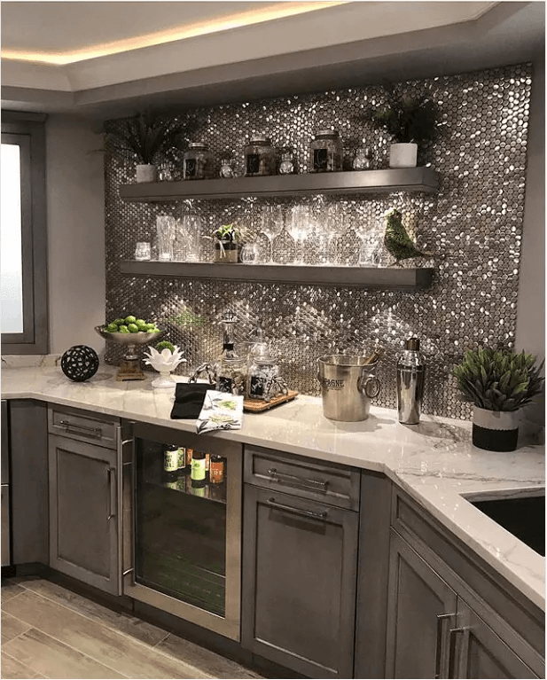 A kitchen with gray cabinets , white counter tops , a refrigerator , and a bar.