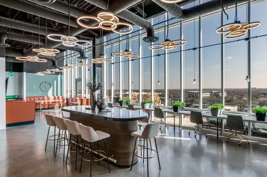 Modern office lounge with tall windows, bar, seating, and city views