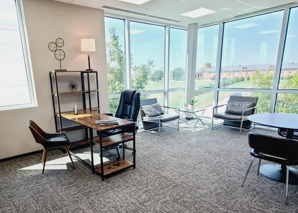 A room with a desk, chairs, tables, and windows.