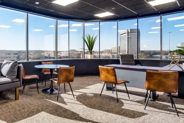 A room with a desk, chairs, a couch, and a large window.
