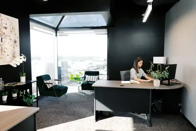 A woman is sitting at a desk in an office with a computer.