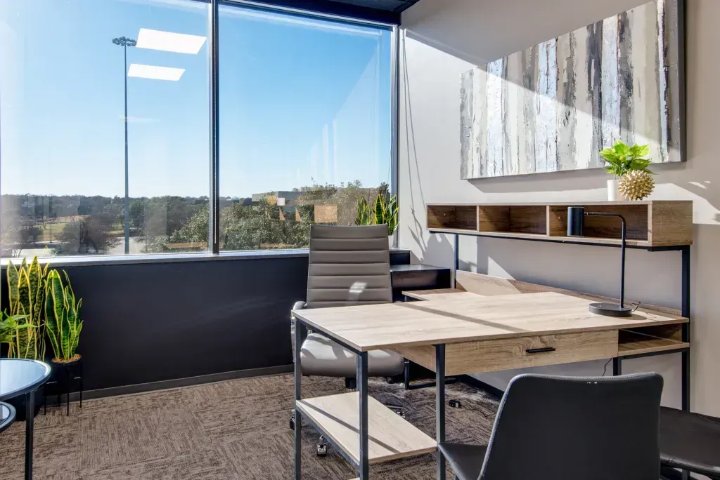 A small office with a desk and chairs and a large window.