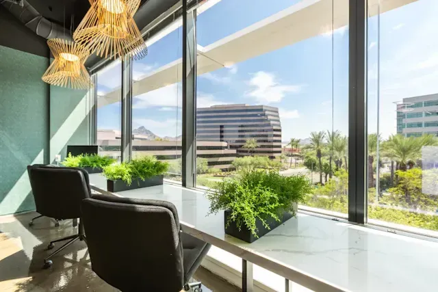 A room with a desk and chairs in front of a large window.
