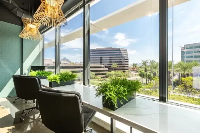 A room with a desk and chairs in front of a large window.