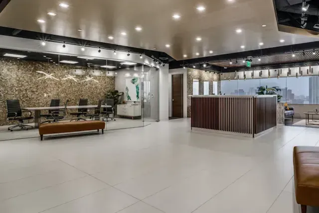 A large room with a reception desk, tables, chairs, and a bench.