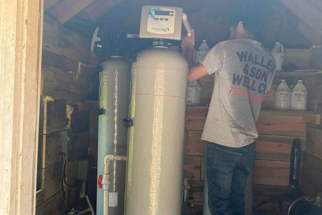 Man working on a water filtration system inside a wooden shed.