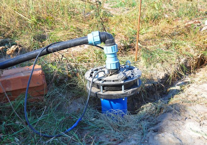 Well pump with black pipe and blue fittings, installed in the ground.