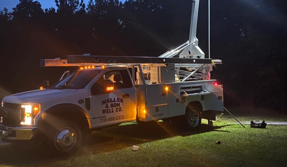 White work truck at night with an extended antenna and lights illuminating the grass.