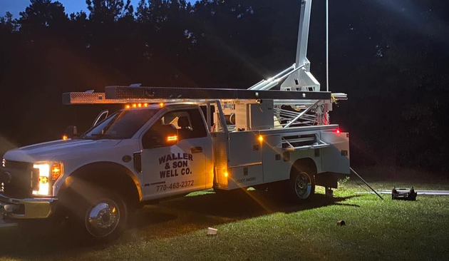 White work truck at night with an extended antenna and lights illuminating the grass.