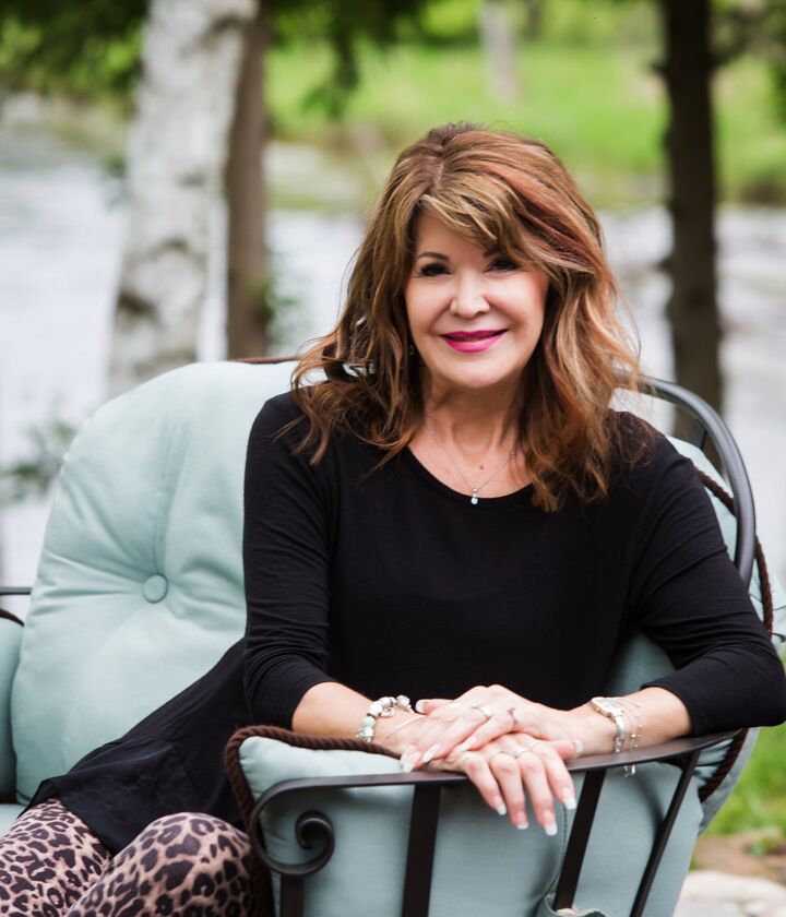 Woman smiling on a patio chair outdoors, wearing a black top with a light blue cushion behind her.