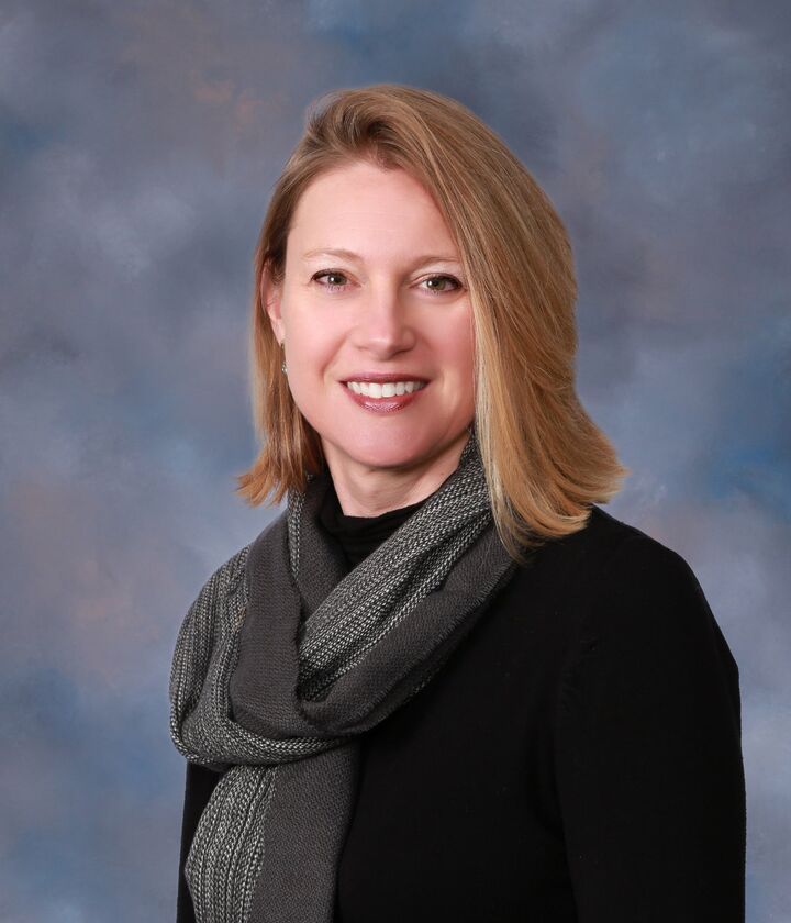 Portrait of a smiling woman in a black top and gray scarf against a blue-gray backdrop