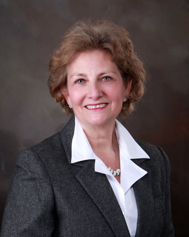 Studio portrait of a smiling woman in a gray blazer and white collared shirt.