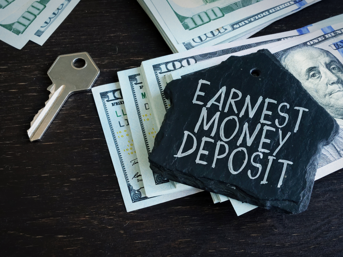 Earnest money deposit sign on black stone beside house keys and cash bills