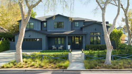 Modern dark-gray two-story house with large windows, front lawn, and trees along the street