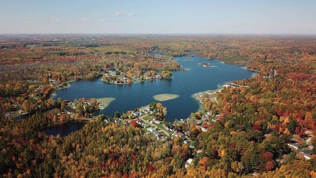 Aerial view of a blue lake surrounded by dense autumn forest with colorful fall foliage.
