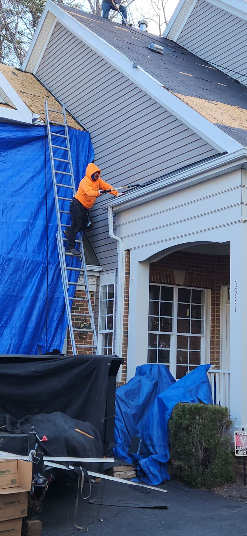 A man is standing on a ladder on the roof of a house.