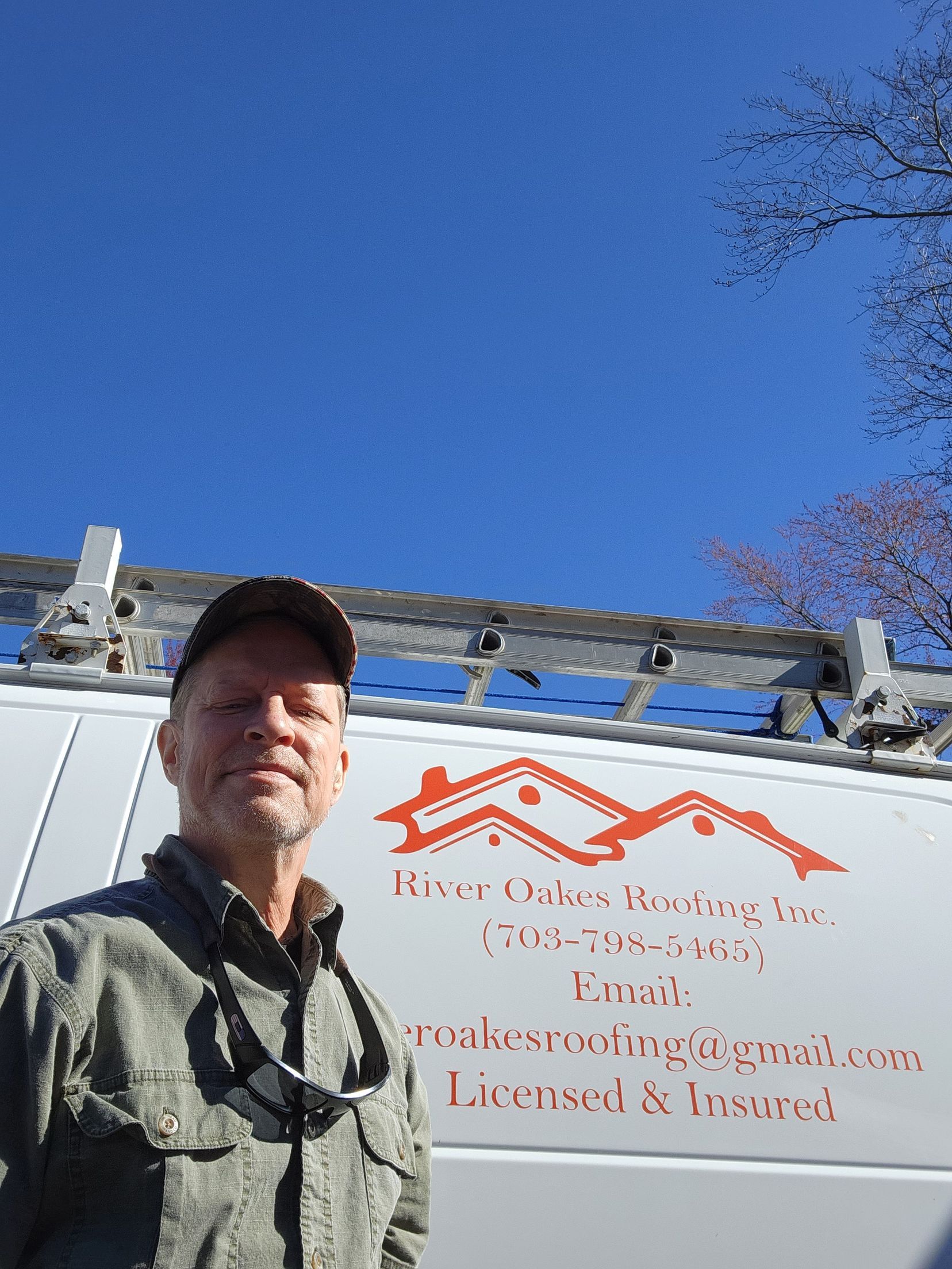 A man is standing in front of a white van with a ladder on top of it.