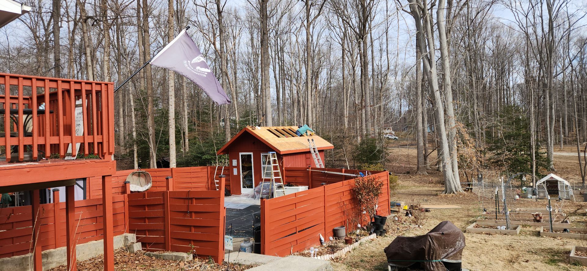 A small red house is surrounded by a wooden fence in the middle of a forest.