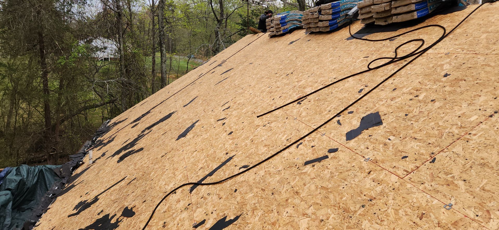 A roof is being built on a hill with trees in the background.