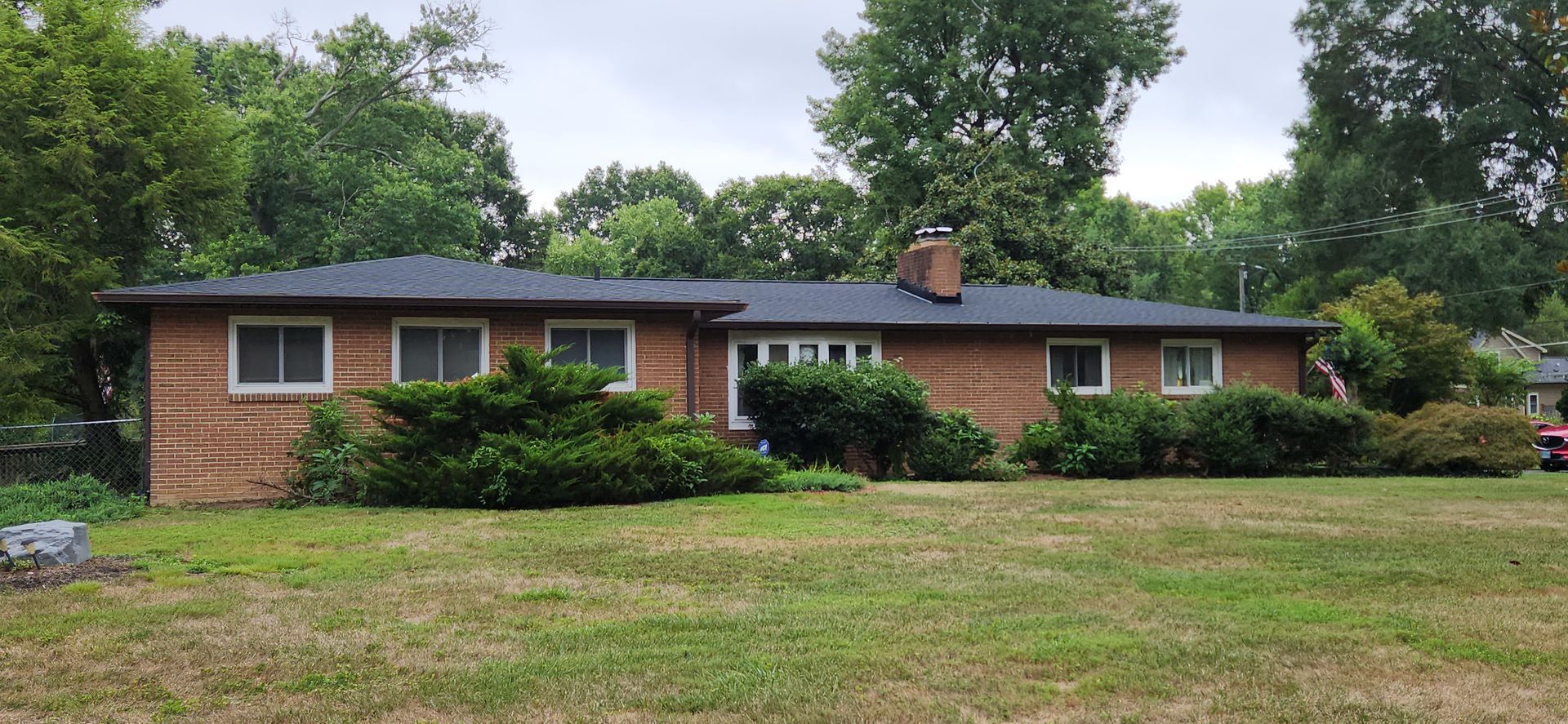 A large brick house with a black roof is sitting on top of a lush green field.