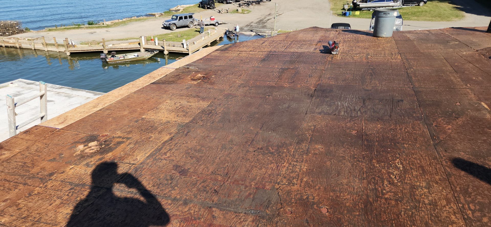 A person is standing on top of a rusty roof overlooking a body of water.