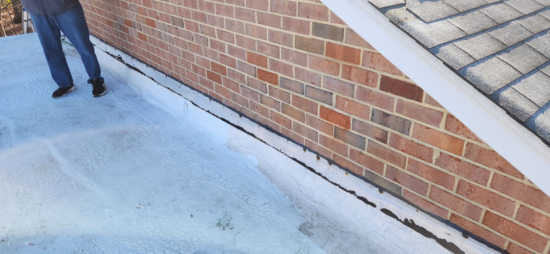 A man is standing next to a brick wall and a roof.