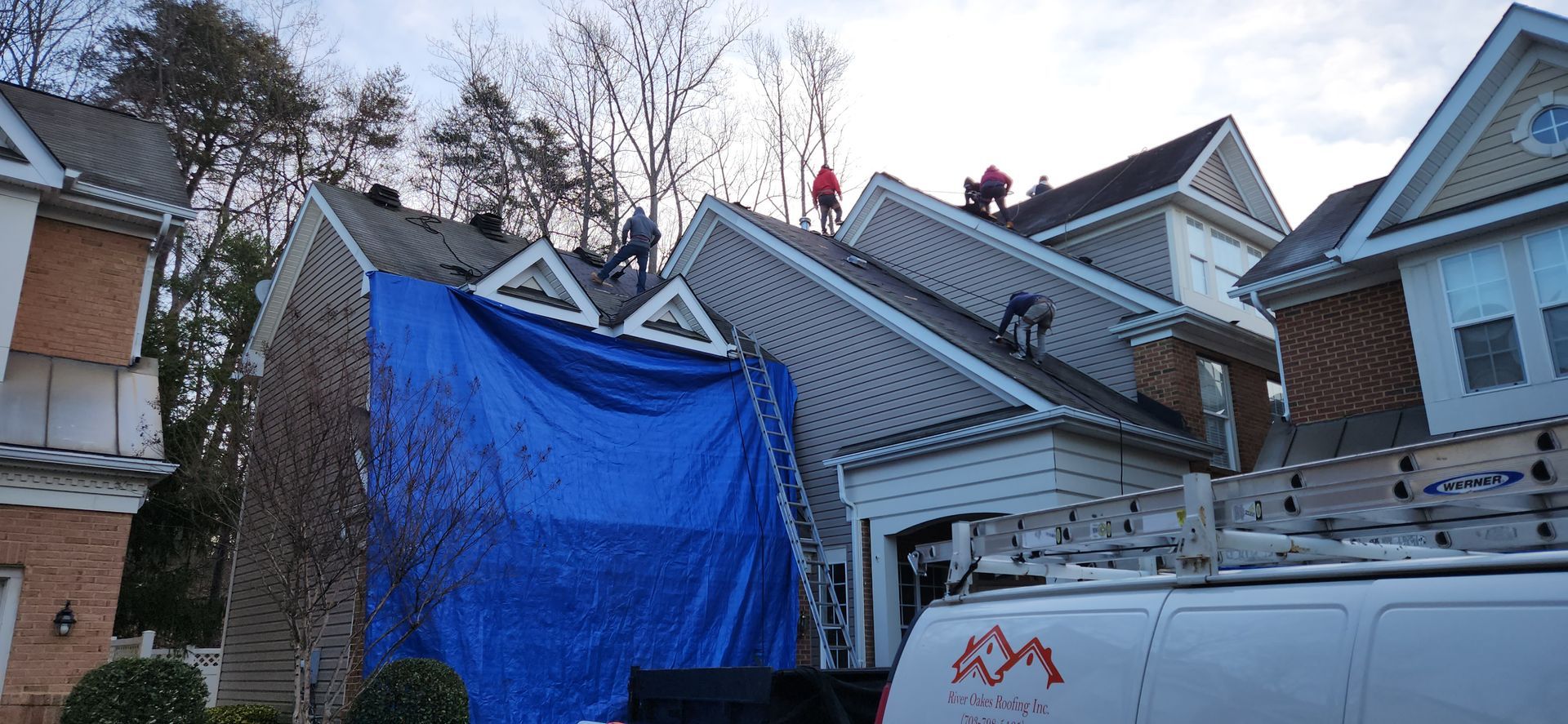 A white van is parked in front of a house with a blue tarp on the roof.