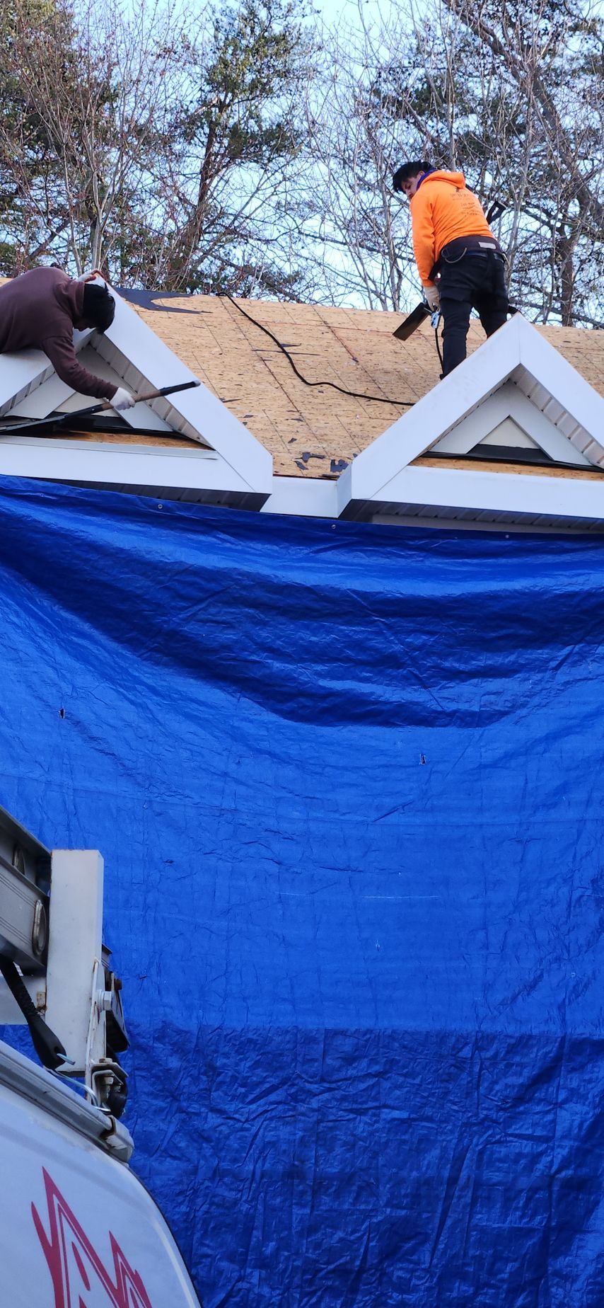 Two men are working on a roof with a blue tarp.