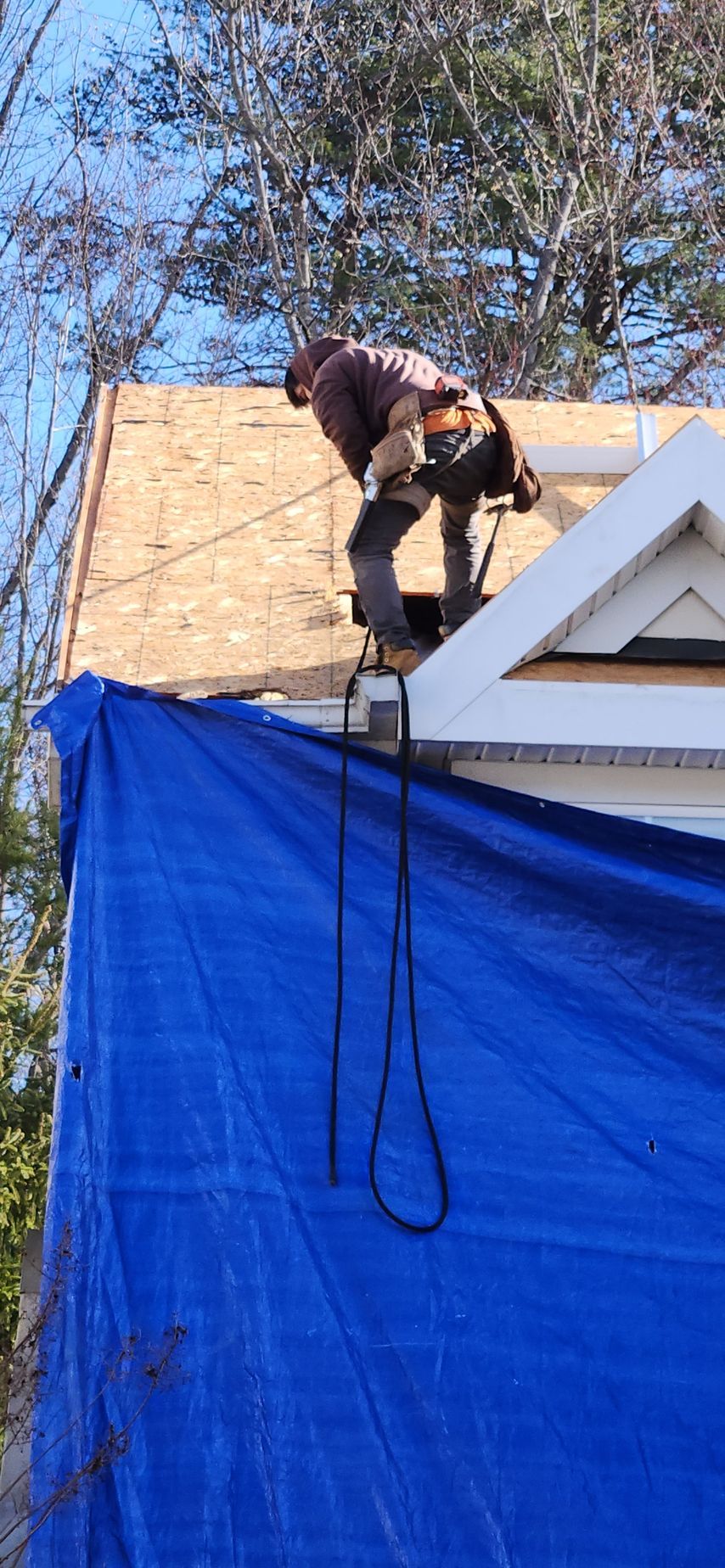 A man is working on the roof of a house with a blue tarp.