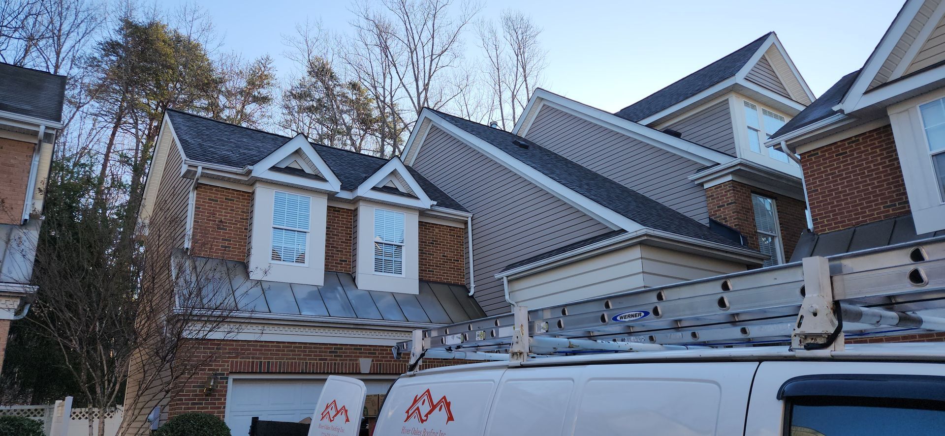 A white van with a ladder on top of it is parked in front of a house.