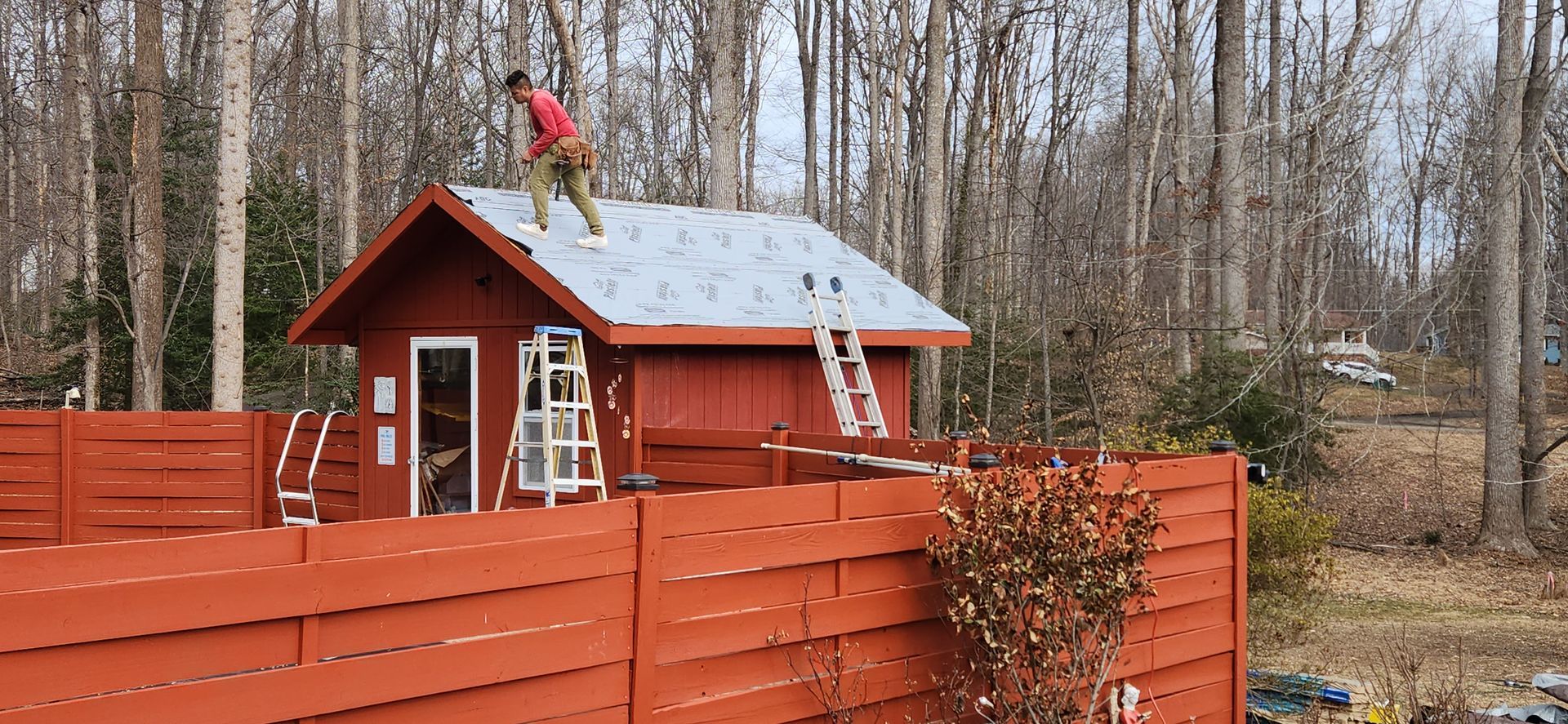 A man is standing on the roof of a red shed.