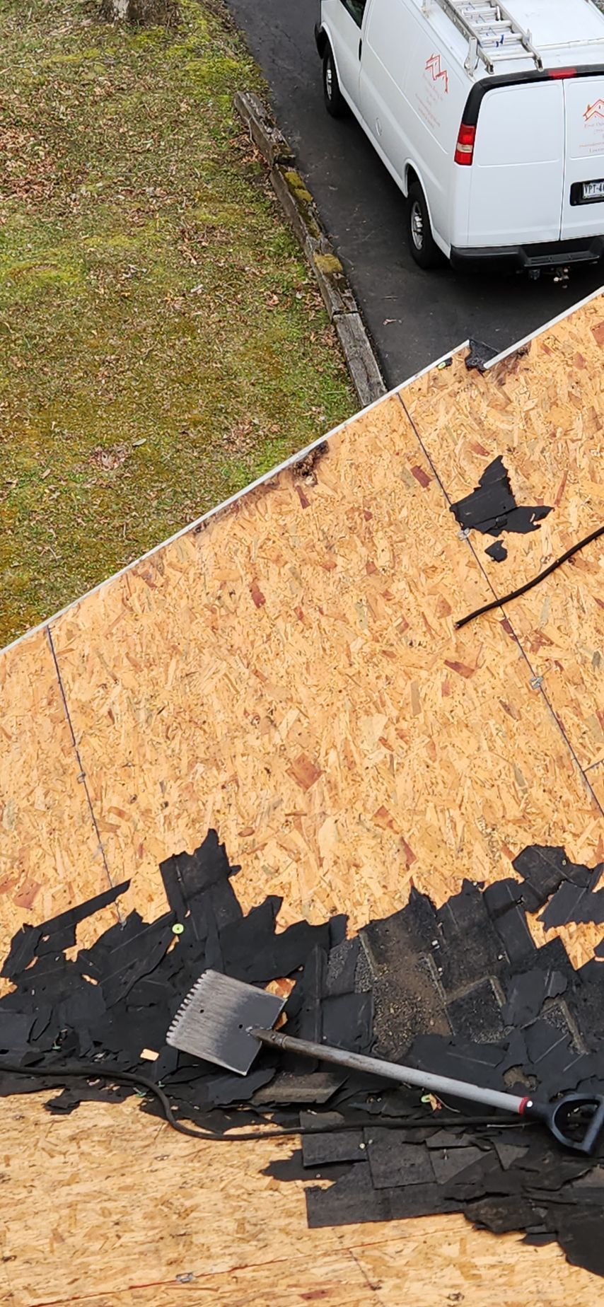 A white van is parked on the side of the road next to a roof that is being repaired.