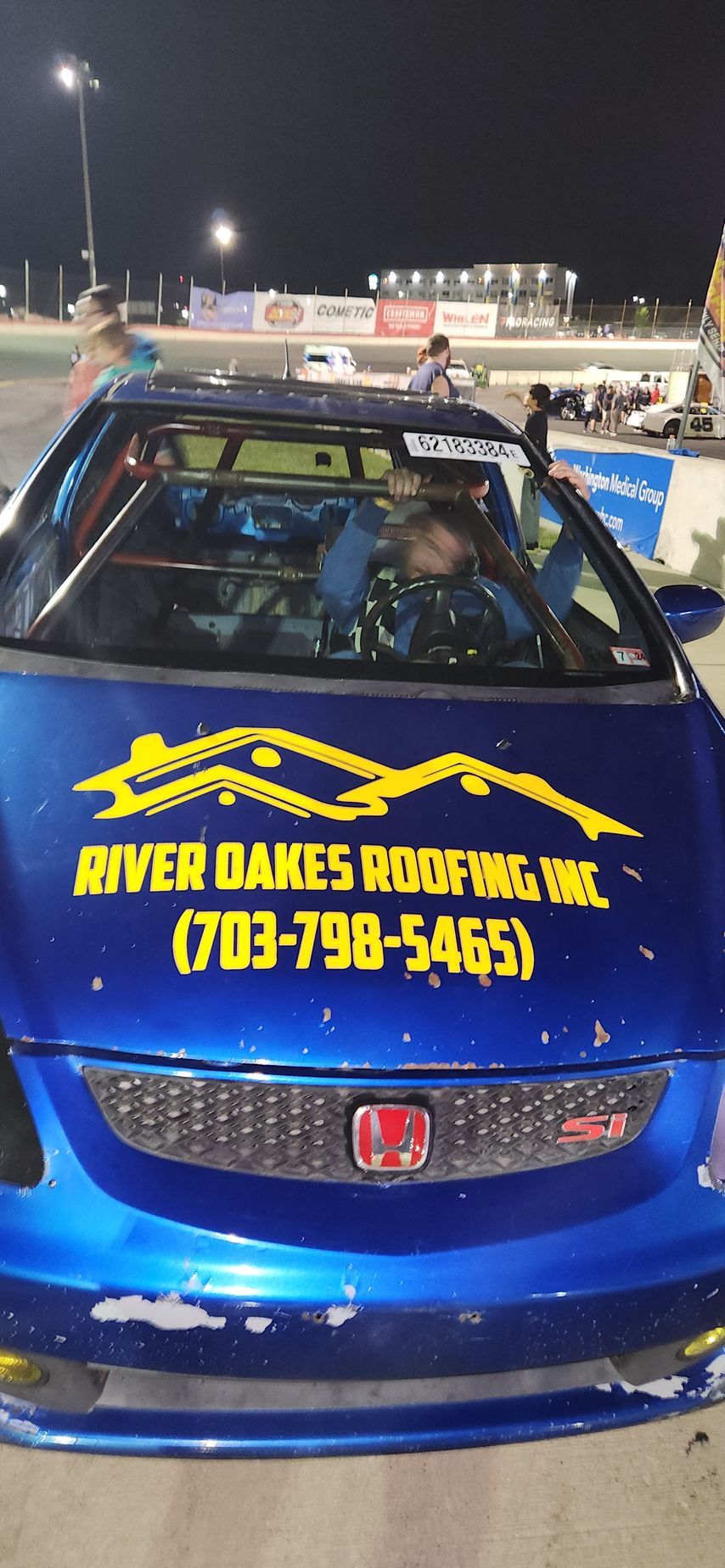 A blue car with a yellow sticker on the front that says river oaks roofing