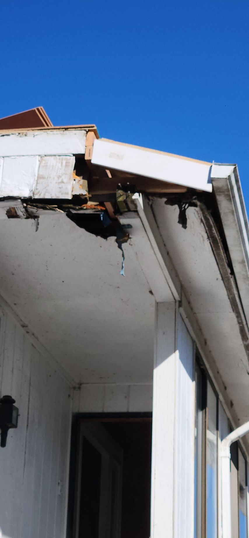 A white house with a roof that has been damaged