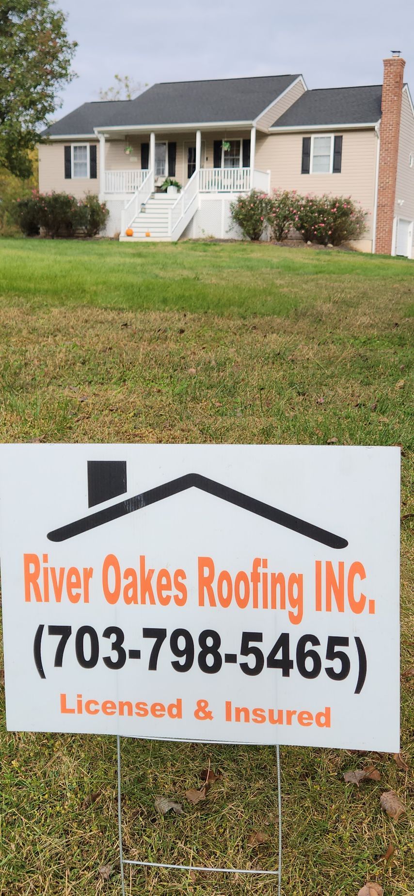 A sign for river oaks roofing inc. is in front of a house.