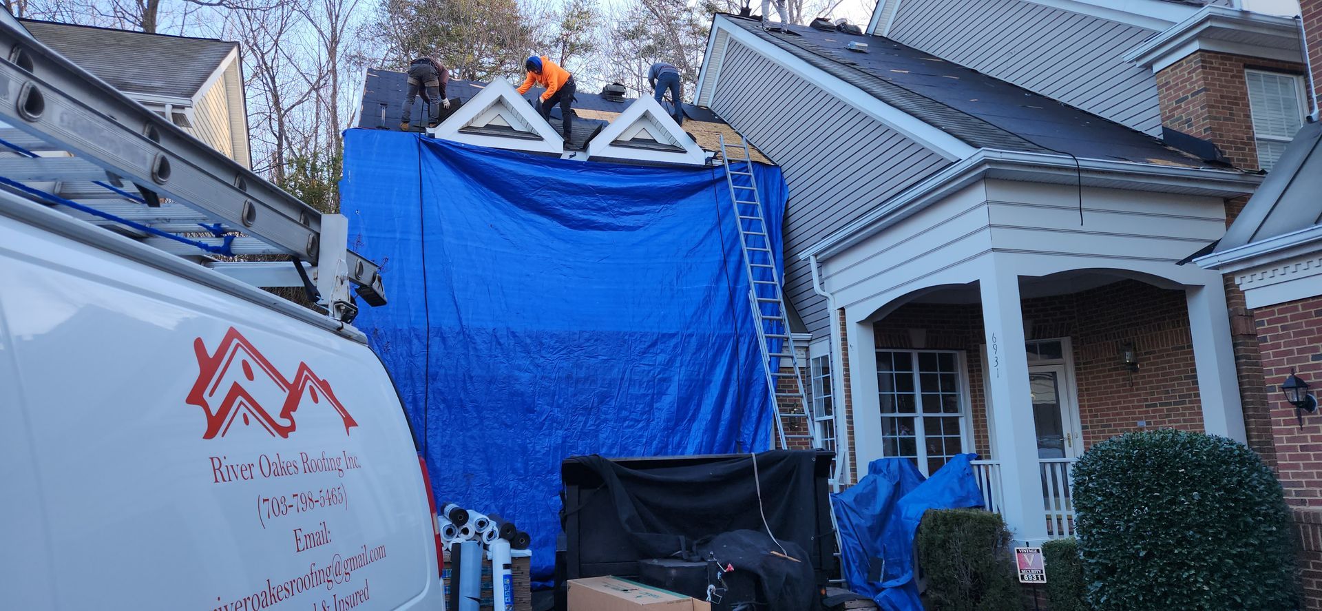 A white van is parked in front of a house with a blue tarp on the roof.
