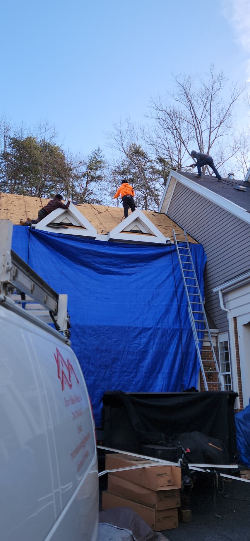 A man is working on the roof of a house covered in a blue tarp.